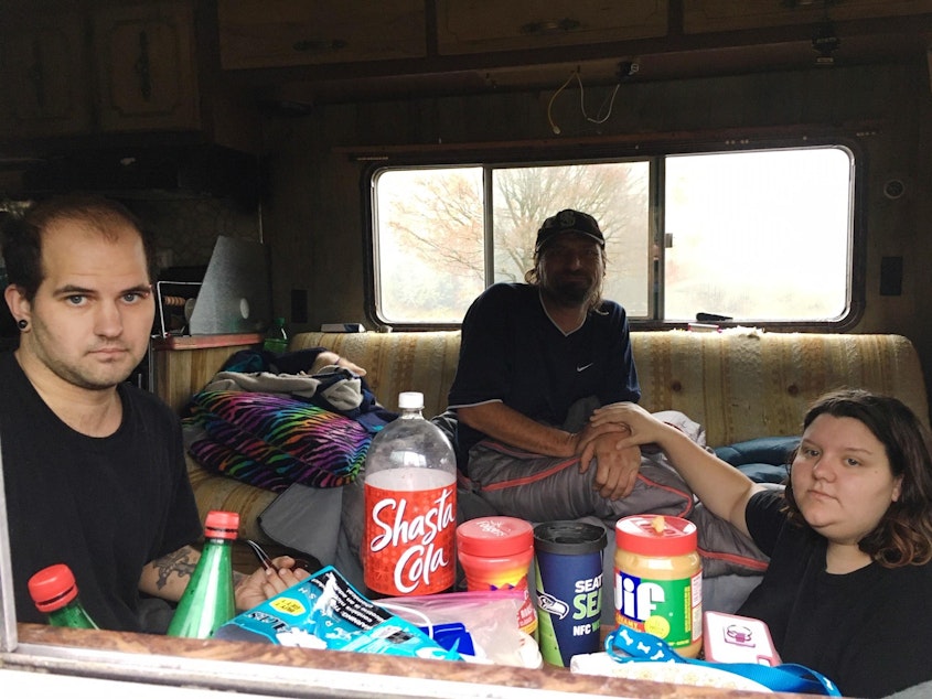 caption: Austin Hall, left, his fiance Victoria Swan and a man who identified himself as Mark Goddard sit in one of the RVs parked on Deschutes Parkway on Washington's Capitol campus.
