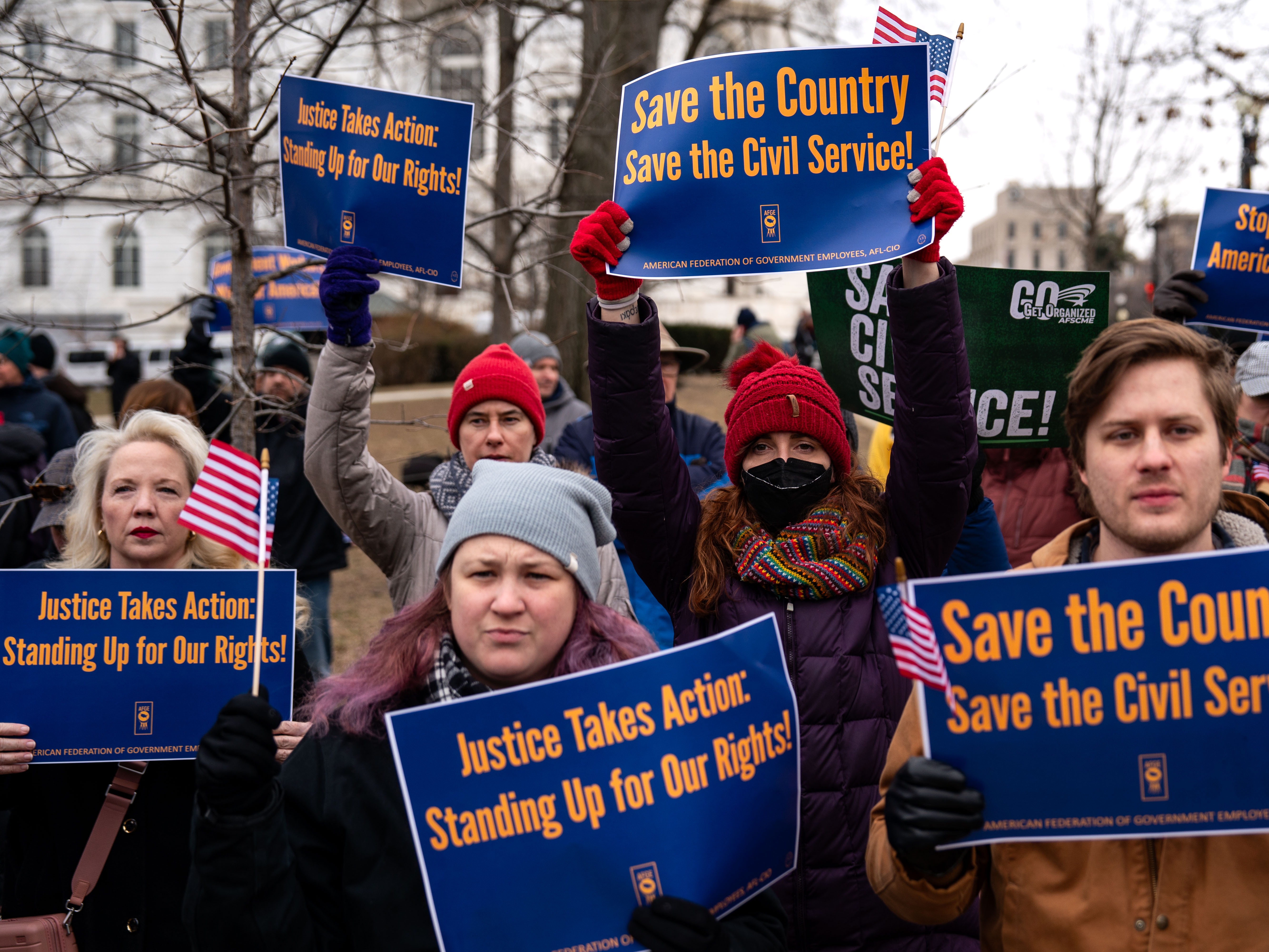 caption: People hold signs during a "Save the Civil Service" rally outside the U.S. Capitol on Feb. 11, 2025 in Washington, D.C.