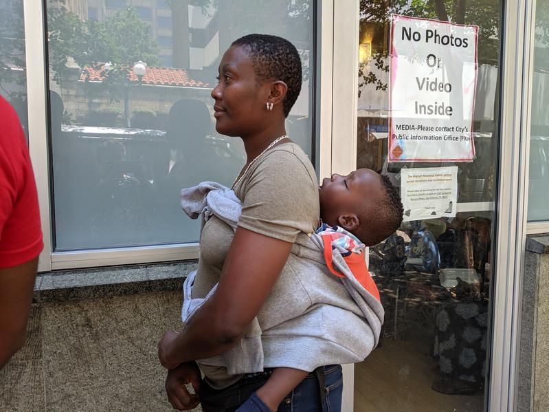 caption: A woman waits in line with her child outside the migrant processing center in San Antonio.