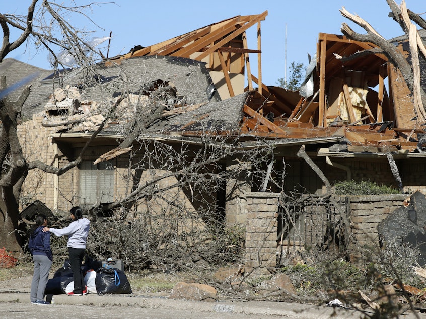 caption: Women stand outside a house damaged by a tornado in the Preston Hollow section of Dallas. The city was still cleaning up after the tornado on Monday.