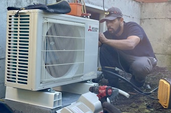 caption: CM Heating technician Saul Benitez installs a heat pump in Shoreline, Washington, on July 28, 2023.
