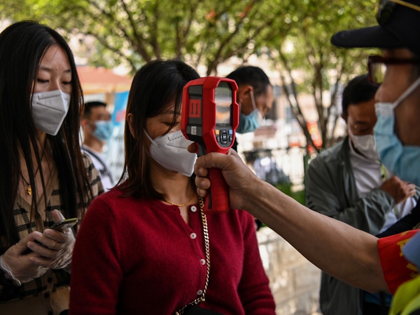 caption: A worker checks a passenger's body temperature on Tuesday after arriving in Wuhan, China. Earlier this week, authorities found at least six new cases of the coronavirus.