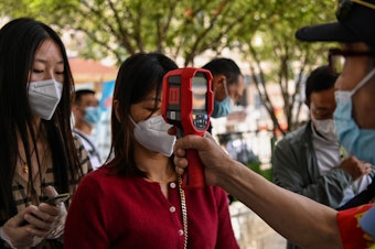 caption: A worker checks a passenger's body temperature on Tuesday after arriving in Wuhan, China. Earlier this week, authorities found at least six new cases of the coronavirus.