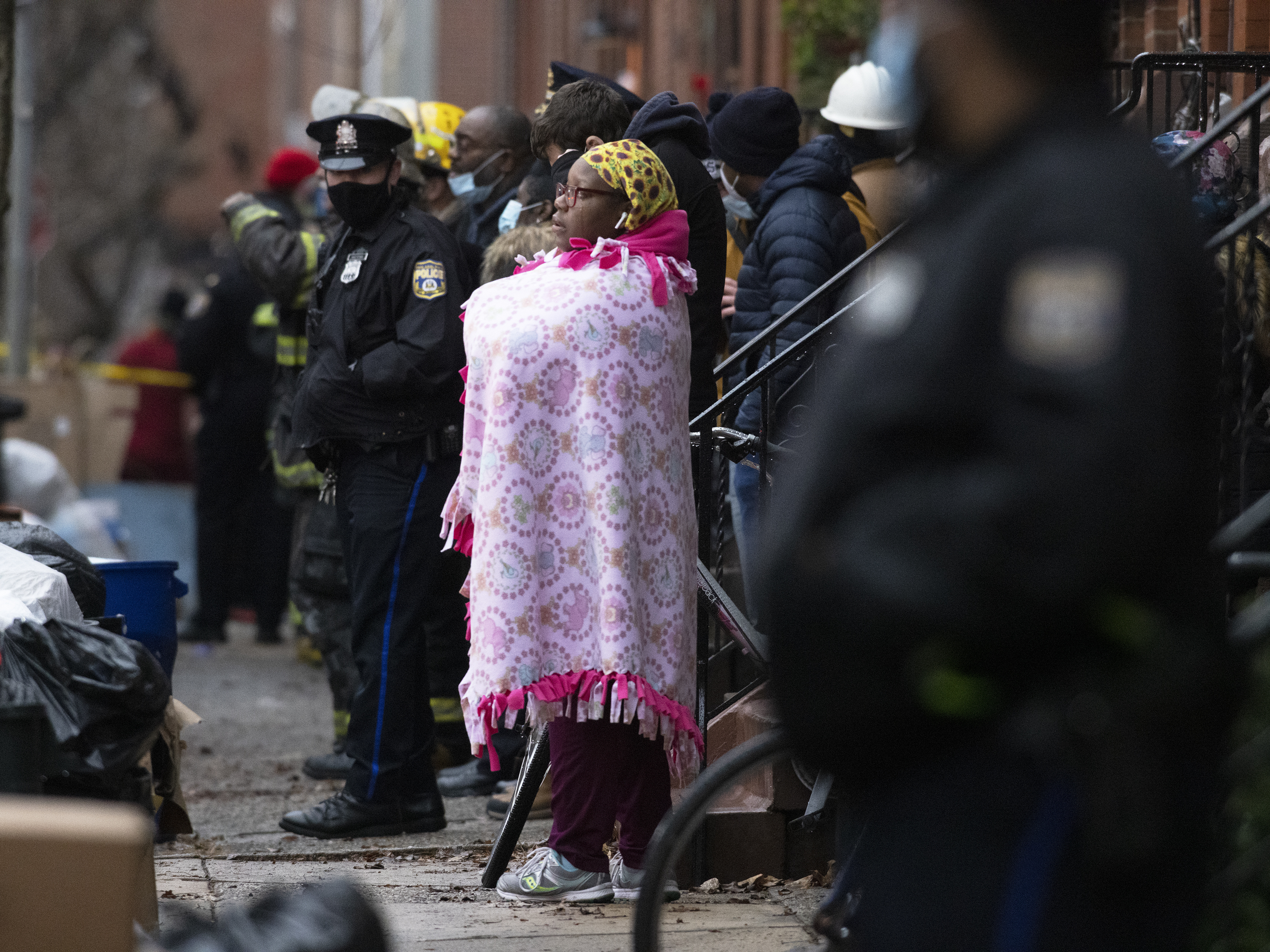 caption: Bystanders watch as the Philadelphia Fire Department works at the scene of a deadly row house fire on Wednesday.
