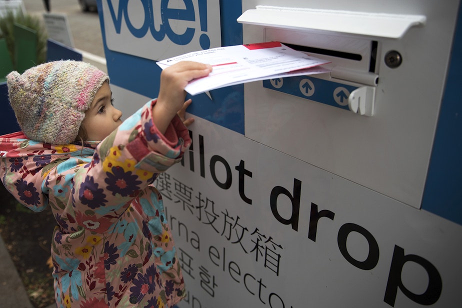 caption: FILE: Olivia Blanchard, 4, drops a ballot into the ballot drop box outside of the Seattle Public Library on Tuesday, November 7, 2017, in Ballard. 