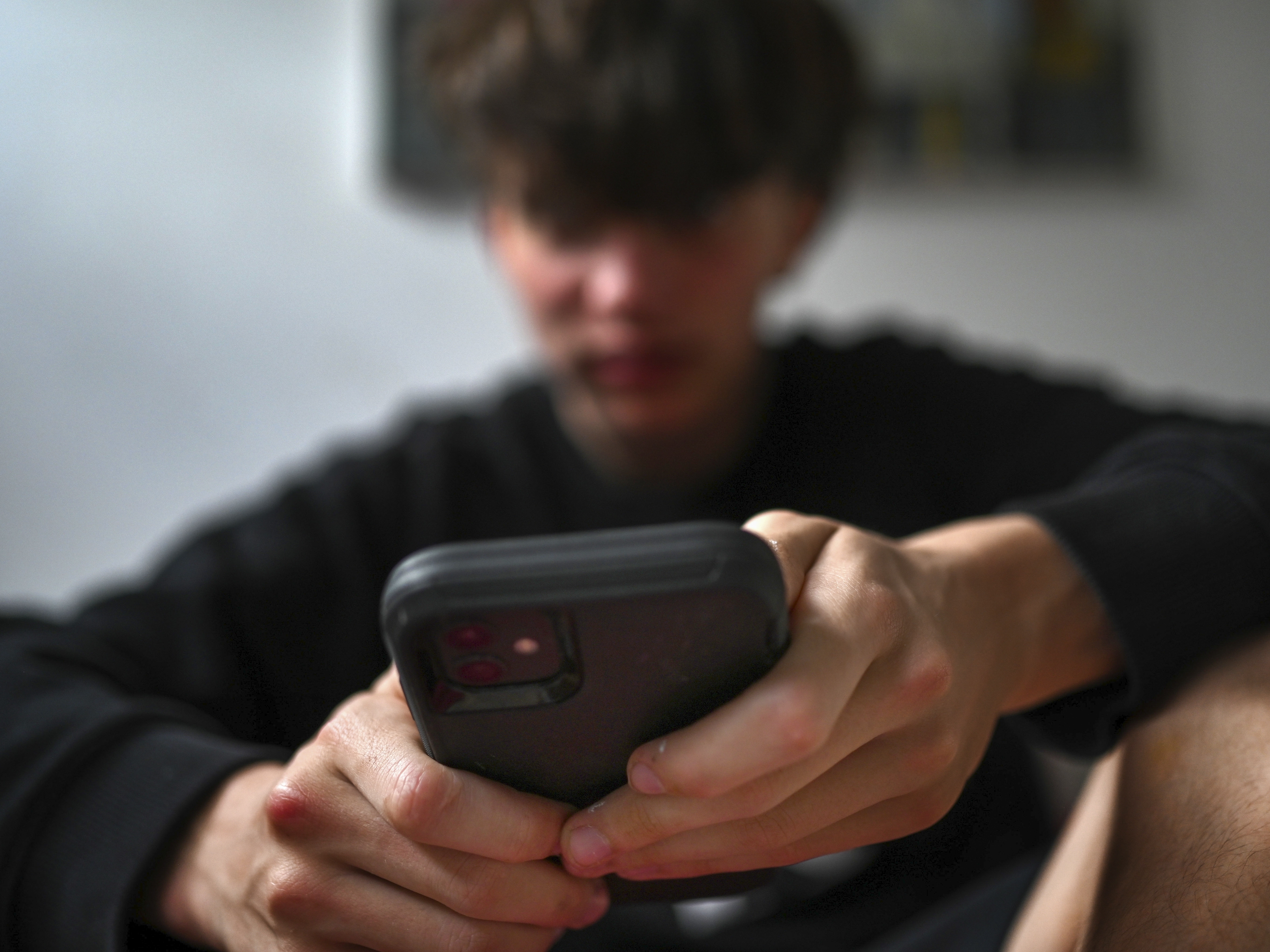 caption: A teenager uses his mobile phone to access social media in Sydney on Nov. 13.