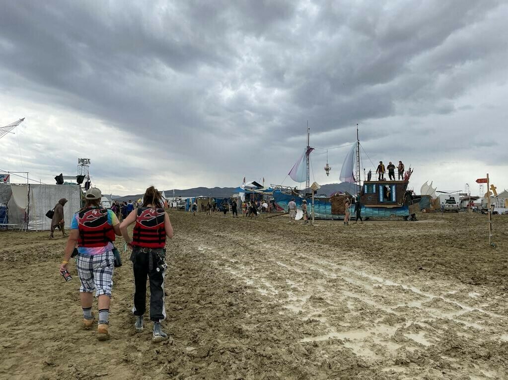 caption: Burning Man attendees walk through a muddy desert plain on Saturday, after heavy rains pelted the annual Nevada festival.