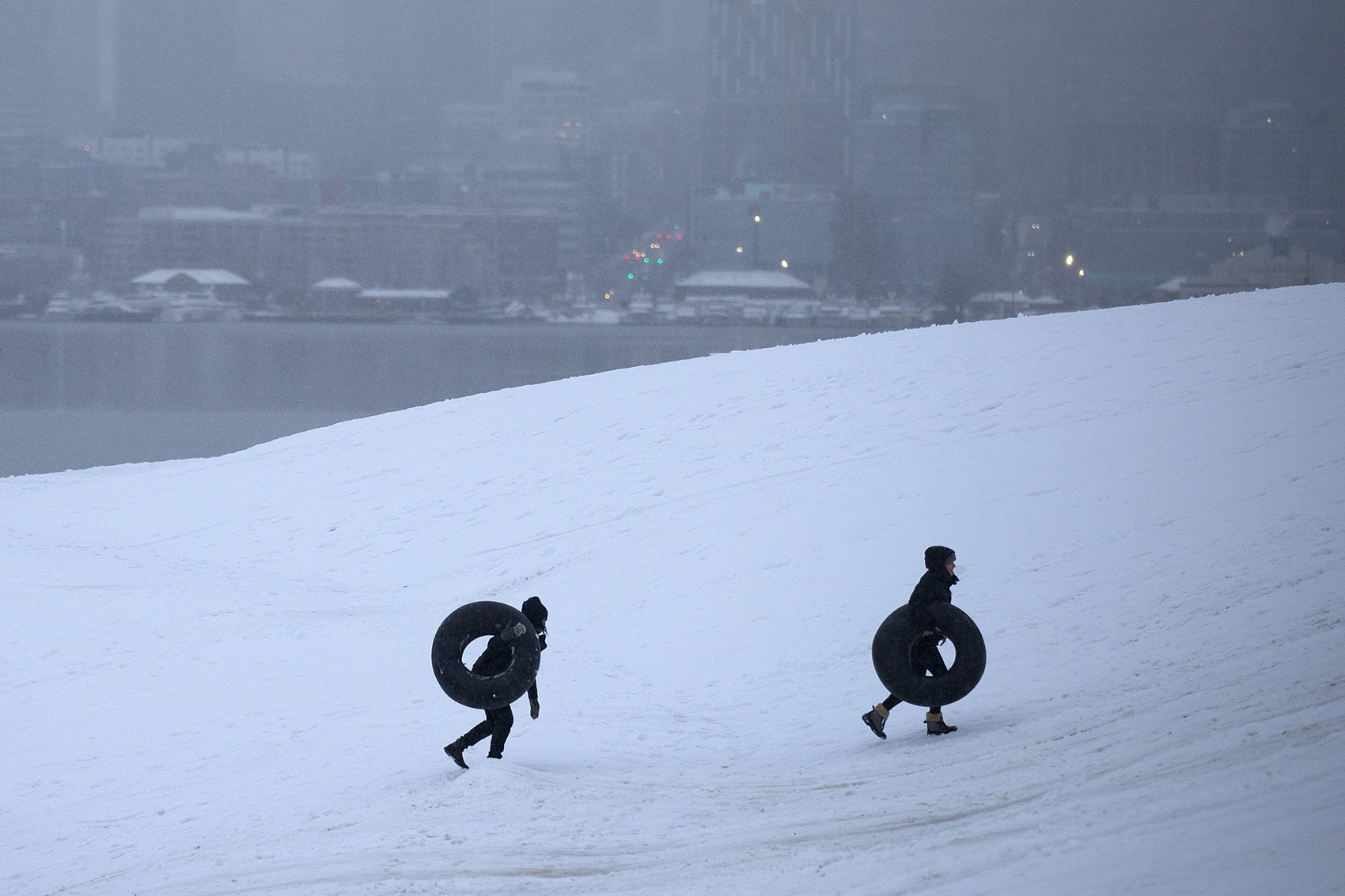caption: Snow tubes are carried up the hill at Gas Works Park on Monday, February 11, 2019, as snow falls in Seattle. 