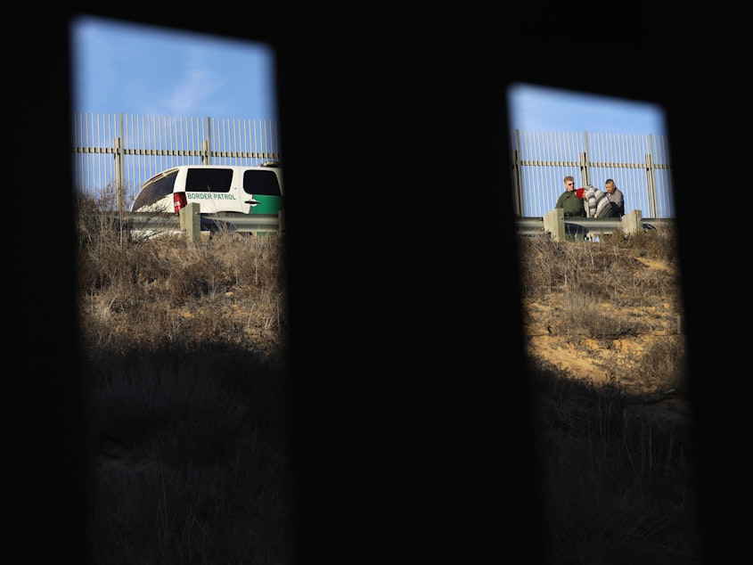 caption: A U.S. Border Patrol agent takes an immigrant into custody in December 2018. Numerous members of the migrant caravan crossed over from Tijuana to San Diego but were quickly taken into custody by U.S. Border Patrol agents.