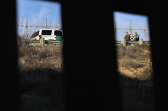 caption: A U.S. Border Patrol agent takes an immigrant into custody in December 2018. Numerous members of the migrant caravan crossed over from Tijuana to San Diego but were quickly taken into custody by U.S. Border Patrol agents.