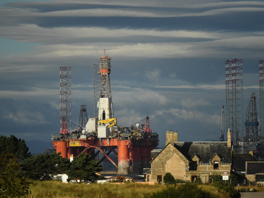 caption: An oil rig towers over houses in Nigg, Scotland, on September 8. Major players in the oil industry expect depressed oil demand and low prices to continue well into next year.