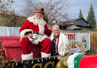 caption: Tom Carmody as Santa this year. During the coronavirus pandemic, he's been sitting on a trailer that his elf friend tows him around on so he can wave hello to the kids at a safe distance. (Courtesy)