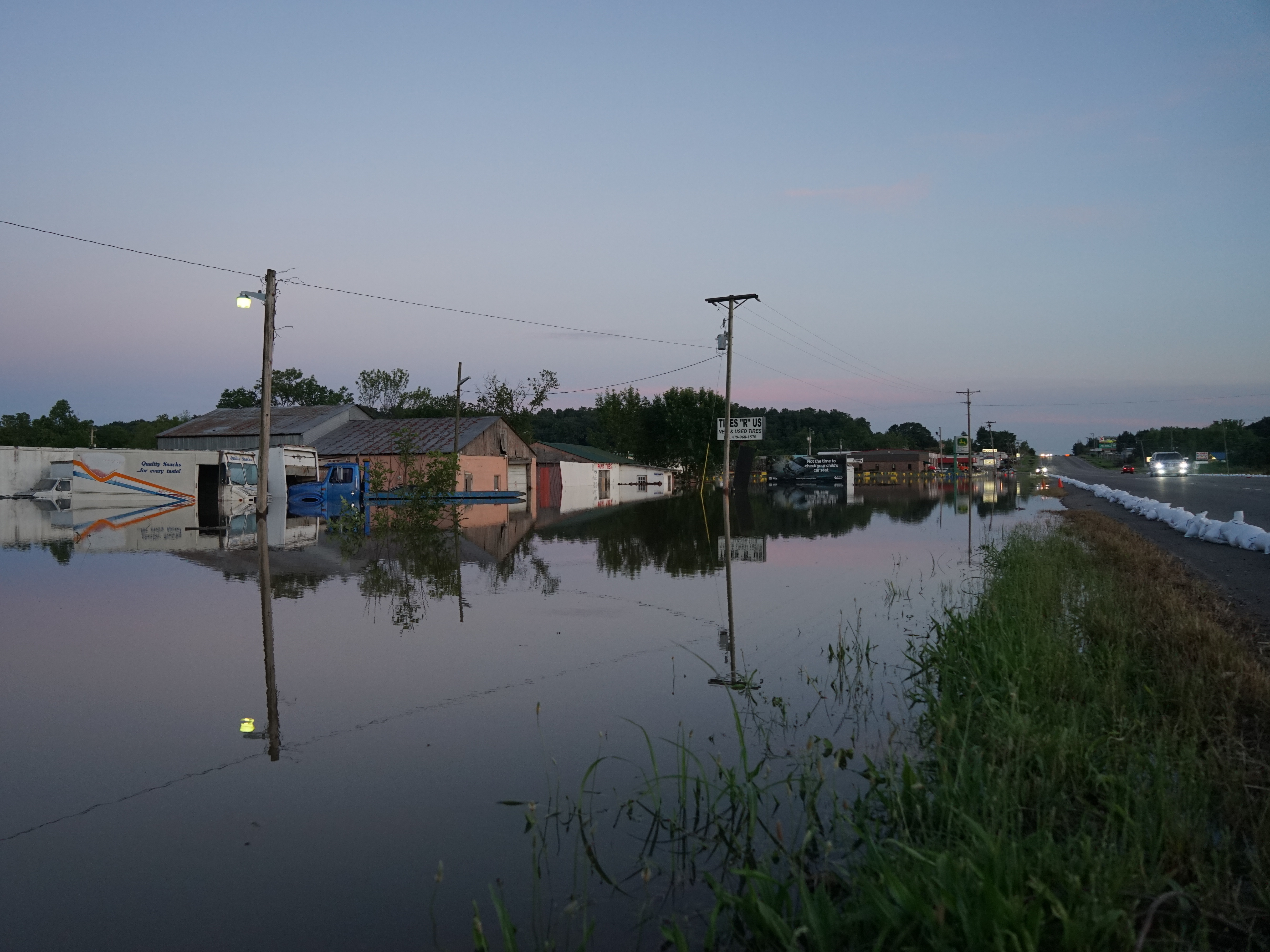 caption: Floodwaters from the Arkansas River line either side of a road in Russellville, Ark., in late May, engulfing businesses and vehicles.
