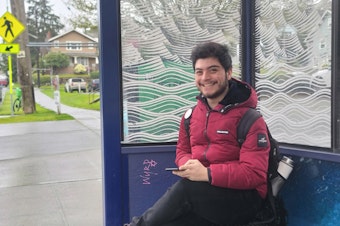 caption: Fabian Hernandez-Angel at the bus stop he uses to return home from school on April 20, 2023 at Seattle Pacific University.