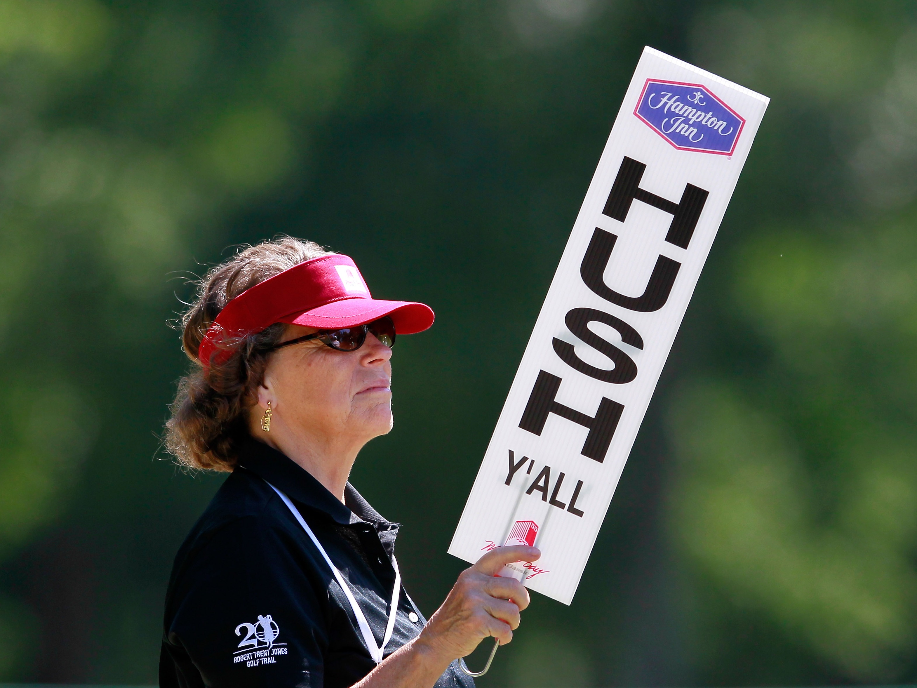 caption: The word "y'all" has spread beyond the South, thanks in part to its blend of polite respect and folksy inclusivity. Here, a golf tournament volunteer holds a "Hush Y'all" sign at the Mobile Bay LPGA Classic in Mobile, Ala., in 2012.