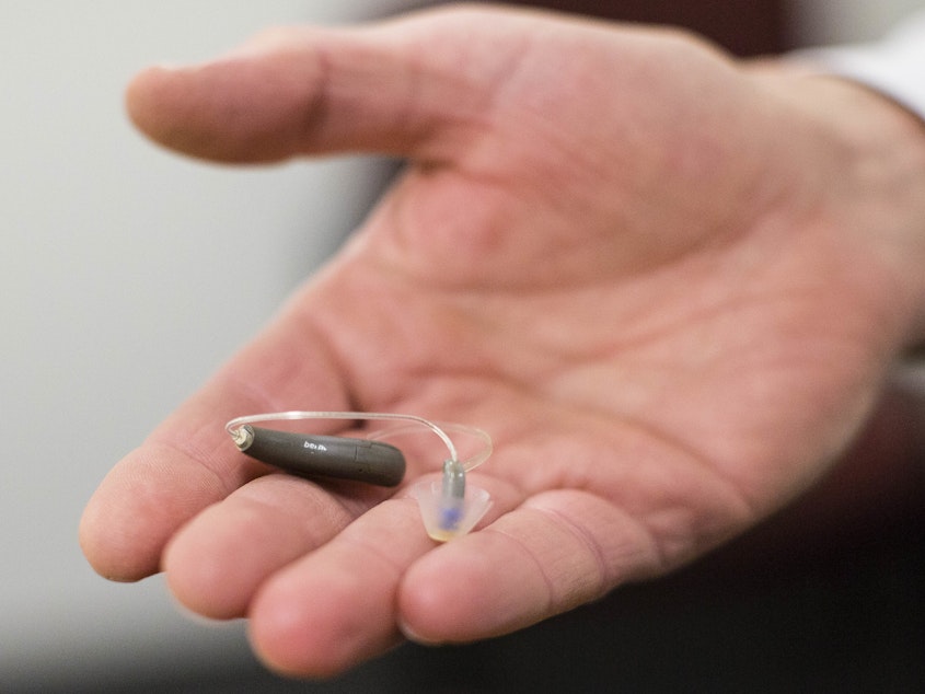 caption: The FDA is moving to approve OTC hearing aids, in a change that lawmakers and advocates have long called for. Here, a man displays his hearing aid before taking part in a meeting.