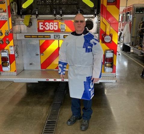 caption: Firefighter Jim Wilson models a protective gown he made out of construction-grade vapor barrier.