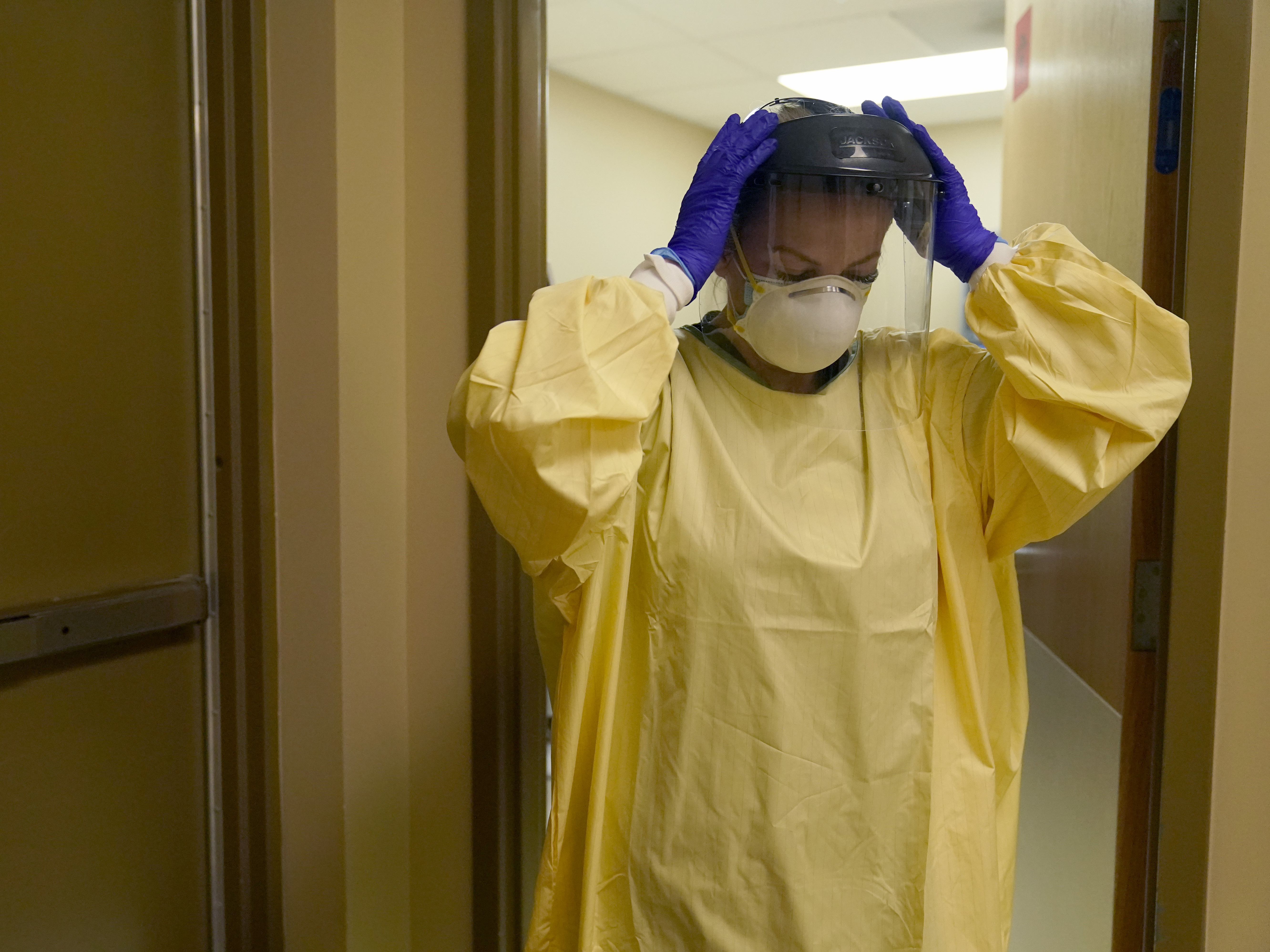 caption: A nurse puts on personal protective equipment as she prepares to treat a COVID-19 patient at a rural Missouri hospital last month.