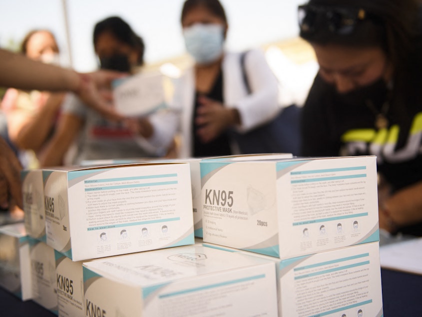 caption: People receive boxes of KN95 face masks during a back to school event offering school supplies, COVID-19 vaccinations, face masks, and other resources for children and their families at the Weingart East Los Angeles YMCA in August.