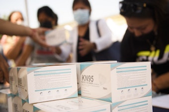 caption: People receive boxes of KN95 face masks during a back to school event offering school supplies, COVID-19 vaccinations, face masks, and other resources for children and their families at the Weingart East Los Angeles YMCA in August.