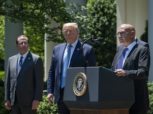 caption: Then-Health and Human Services Secretary Alex Azar (left) and President Donald Trump listen as Moncef Slaoui of Operation Warp Speed speaks about the crash program to develop a COVID-19 vaccine in the White House Rose Garden on May 15, 2020.