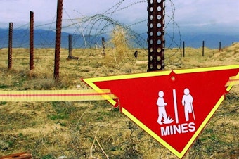 caption: An international sign warning about mines hangs beside a minefield at Bagram Air Base in Afghanistan in 2002.
