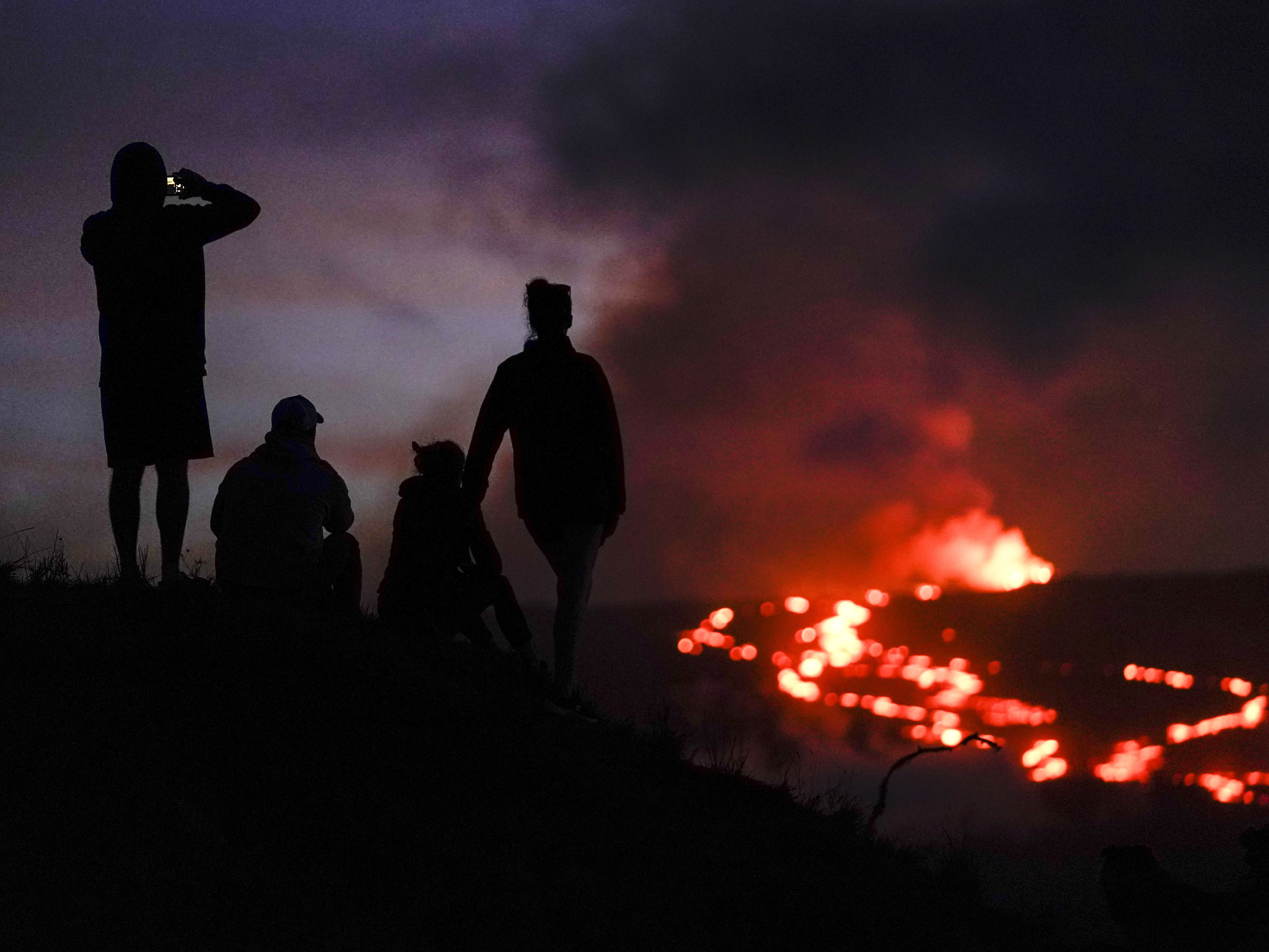 caption: People watch lava from the Mauna Loa volcano on Dec. 1. U.S. scientists declared Tuesday that two active Hawaii volcanoes — one where lava destroyed hundreds of homes in 2018 and another where lava recently stalled before reaching a crucial Big Island highway — have stopped erupting.