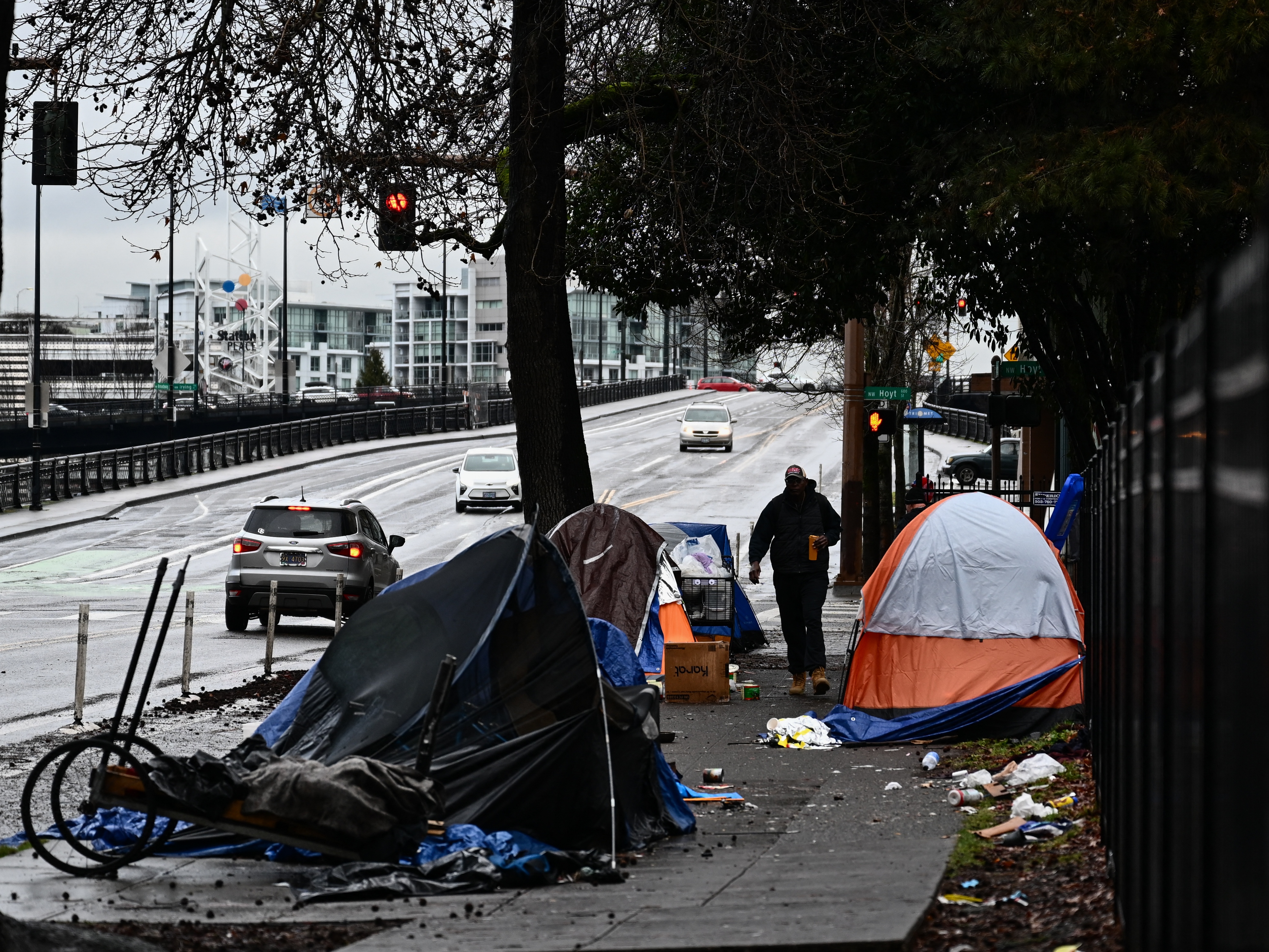 caption: A pedestrian walks past a tent encampment in Portland, Ore., on Jan. 24, 2024. President Trump has promised to sweep homeless Americans out of cities in part by forcing many into "long-term institutional settings." Experts on homelessness and civil liberties have voiced alarm at the proposal.