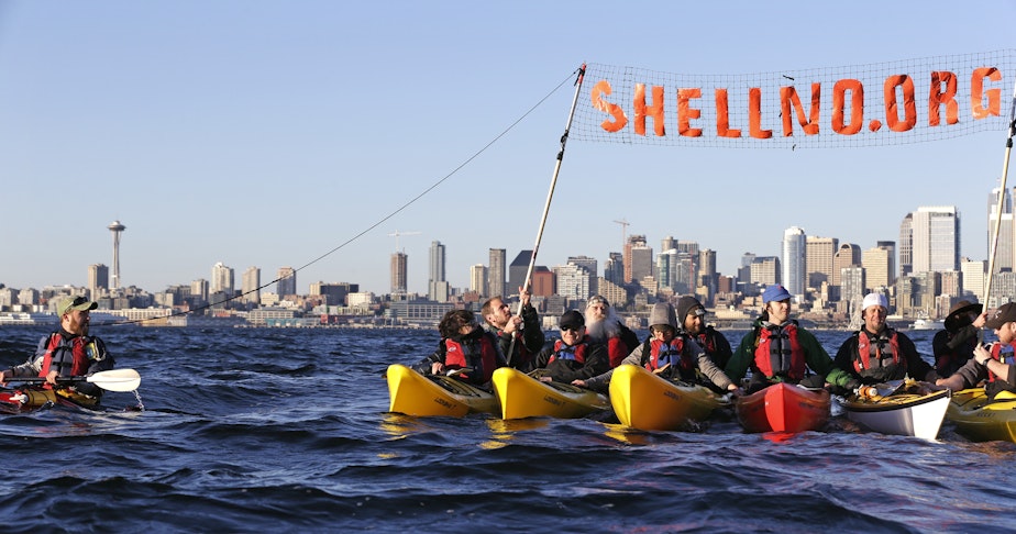 caption: A group of kayakers rafted together work to pull up a protest sign as they practice for an upcoming demonstration against Arctic oil drilling, in Elliott Bay on April 16, 2015.