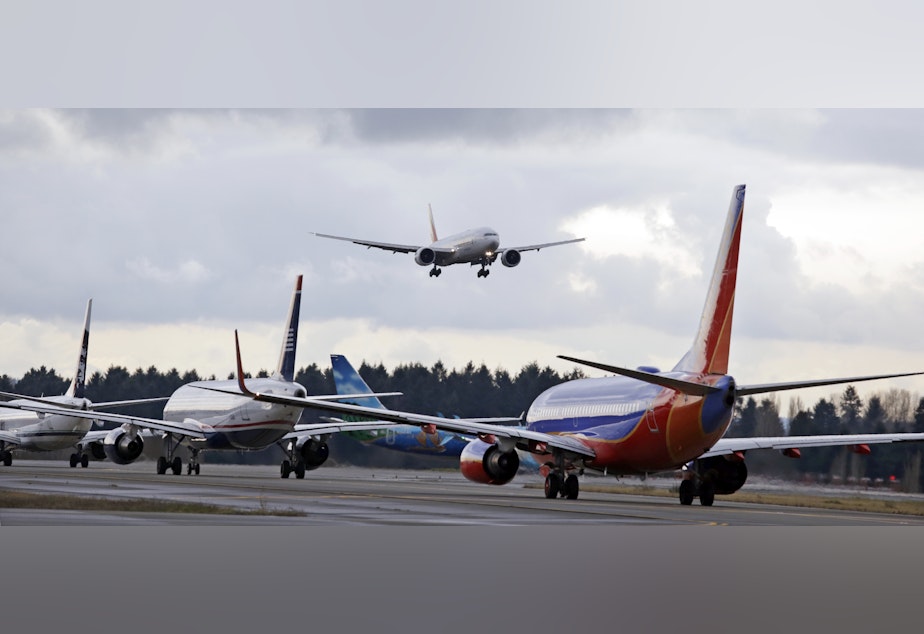 caption: One passenger jet comes in for a landing and in view of a line of planes waiting to takeoff, Wednesday, Dec. 16, 2015, at Seattle-Tacoma International Airport, in SeaTac, Wash.