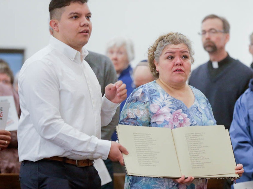 caption: During a service at St. Bridget Catholic Church in Postville, Iowa, last year, Consuelo Lopez (center, right) and her son Pedro carry a book containing the names of those arrested and detained during a 2008 Immigration and Customs Enforcement raid on a local meat processing plant. Consuelo Lopez, who cut meat at the plant, was among those detained and deported.