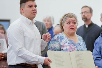 caption: During a service at St. Bridget Catholic Church in Postville, Iowa, last year, Consuelo Lopez (center, right) and her son Pedro carry a book containing the names of those arrested and detained during a 2008 Immigration and Customs Enforcement raid on a local meat processing plant. Consuelo Lopez, who cut meat at the plant, was among those detained and deported.