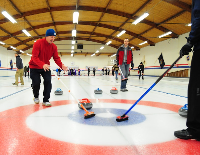 caption: Co-workers move a stone down the ice at Granite Curling Club. The club rents out their facility for group parties.