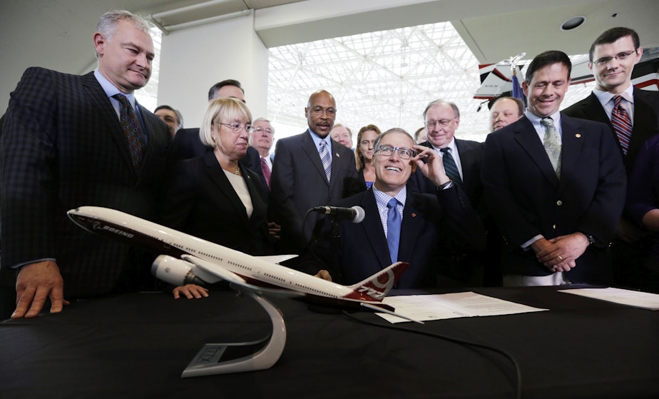 caption: In this Nov. 11, 2013 file photo Washington Gov. Jay Inslee, center, adjusts his glasses as he prepares to sign legislation in Seattle to help keep production of Boeing's new 777X in Washington.