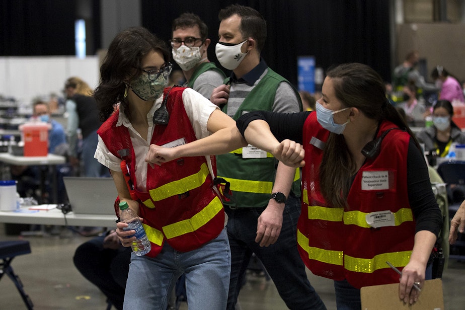 caption: Volunteers celebrate by bumping elbows as the first patients arrive to receive vaccinations against Covid-19 on Saturday, March 13, 2021, at Lumen Field Event Center in Seattle.