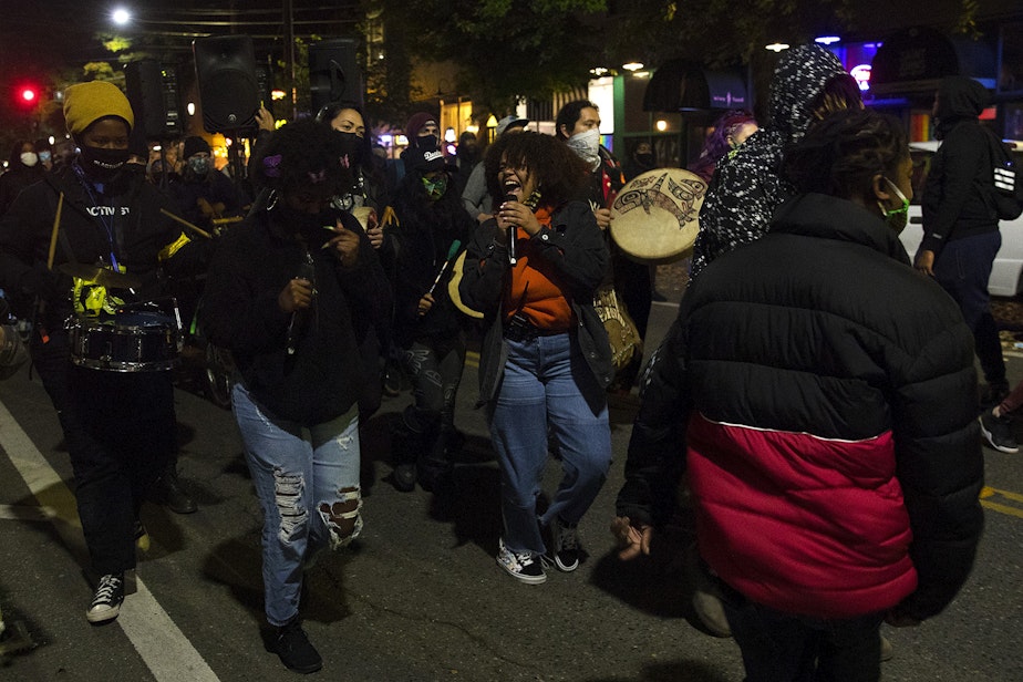 caption: Organizer Tati, center, leads a chant as a large crowd makes their way from Cal Anderson Park to Westlake Park on Monday, October 26, 2020, during the 150th day of protests for racial justice in Seattle.