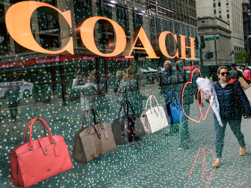 caption: A woman walks past Coach bags in a store window in New York City in 2017.