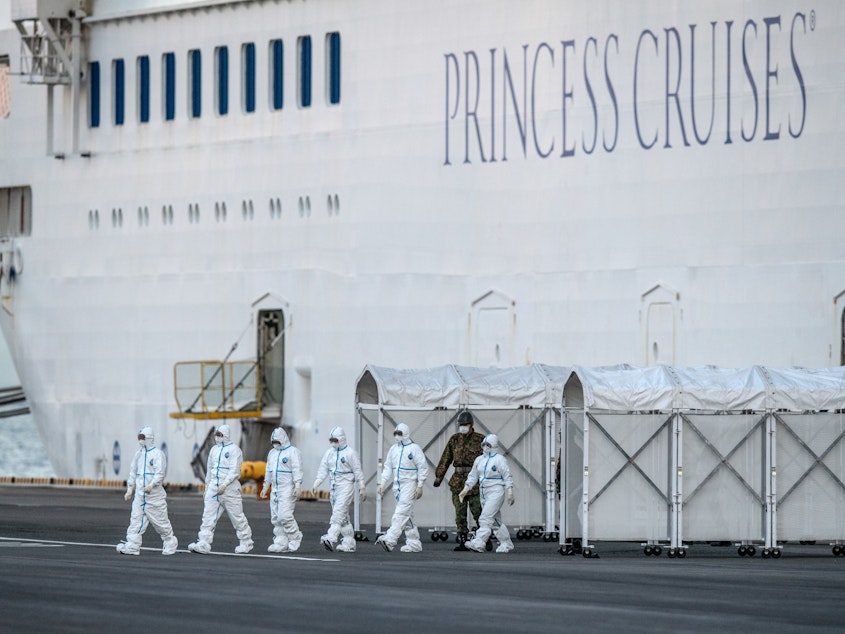 caption: Emergency workers in protective clothing exit the quarantined Diamond Princess cruise ship where it was being resupplied Monday off Yokohama, Japan.