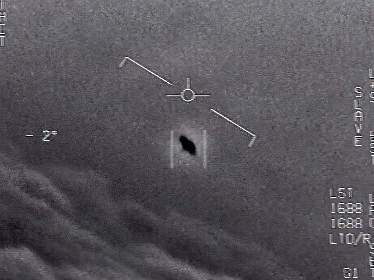 caption: In this image from video provided by the Department of Defense, an unexplained object is seen at center as it soars high among the clouds, traveling against the wind. "There's a whole fleet of them," one naval aviator tells another, though only one indistinct object is shown.