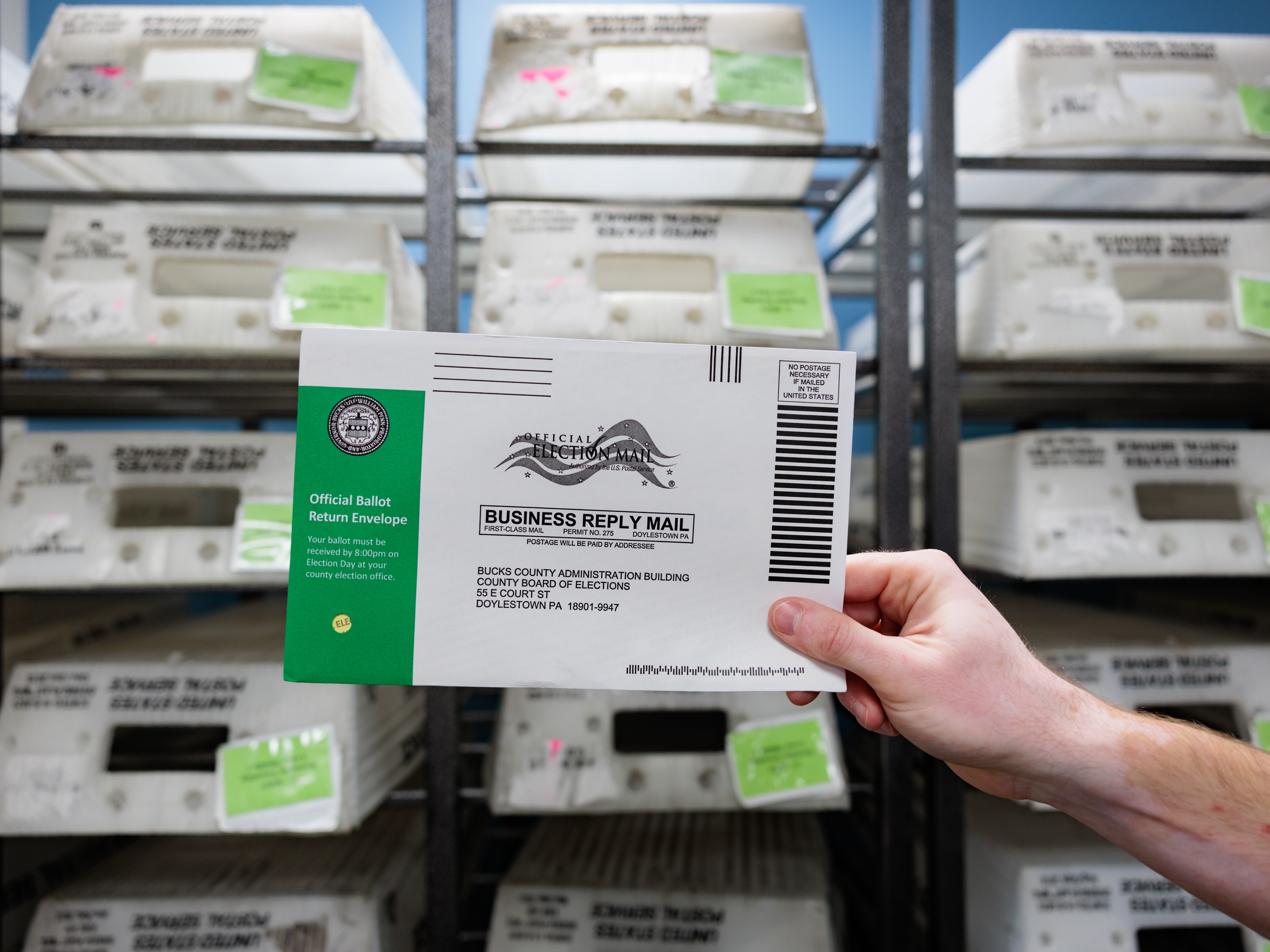 caption: Director of the Board of Elections Tyler Burns holds a test ballot during a mail-in ballot processing demonstration on Sept. 30 in Doylestown, Pa. A fake video purporting to show ballots being destroyed in Bucks County, Pa., showed different envelopes and ballots than the county actually uses.