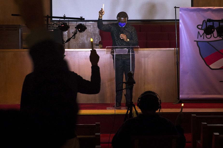 caption: Reverend Carey Anderson holds a candle in the air while leading a 'Mourning into Unity' prayer vigil in response to the coronavirus pandemic on Monday, October 19, 2020, at Seattle's First A-M-E Church on Capitol Hill.