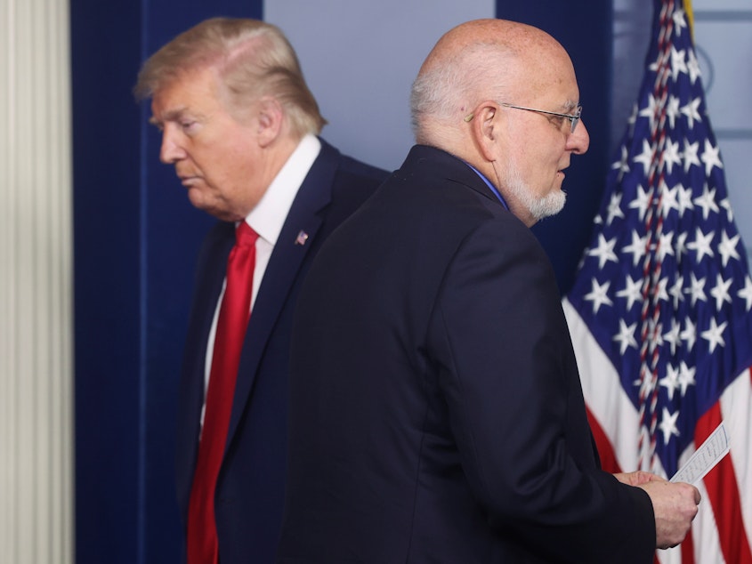 caption: President Trump's administration "is obsessed with magic bullets — vaccines, new medicines, or a hope that the virus will simply disappear," The Lancet says. It urges U.S. voters to elect a new president who will strengthen the Centers for Disease Control. Here, CDC Director Robert Redfield and Trump are seen at a coronavirus task force briefing at the White House last month.