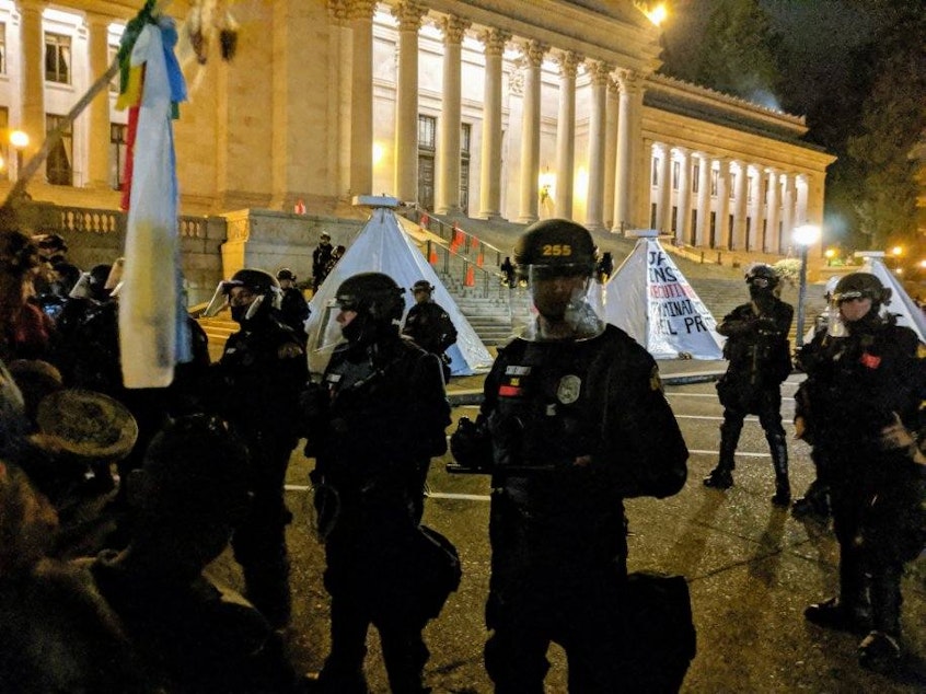 caption: Police in riot gear moved on the protest the morning of September 25th, 2019 to clear out structures at the capitol steps. Indigenous climate activists are demanding Governor Jay Inslee declare a climate emergency.