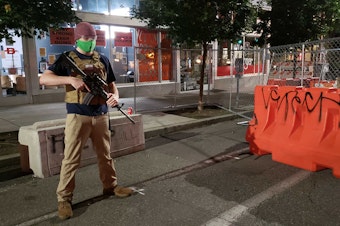 caption: A guard carrying an AR-15 rifle stands at the entrance to the CHAZ at 12th and Pike Street. 