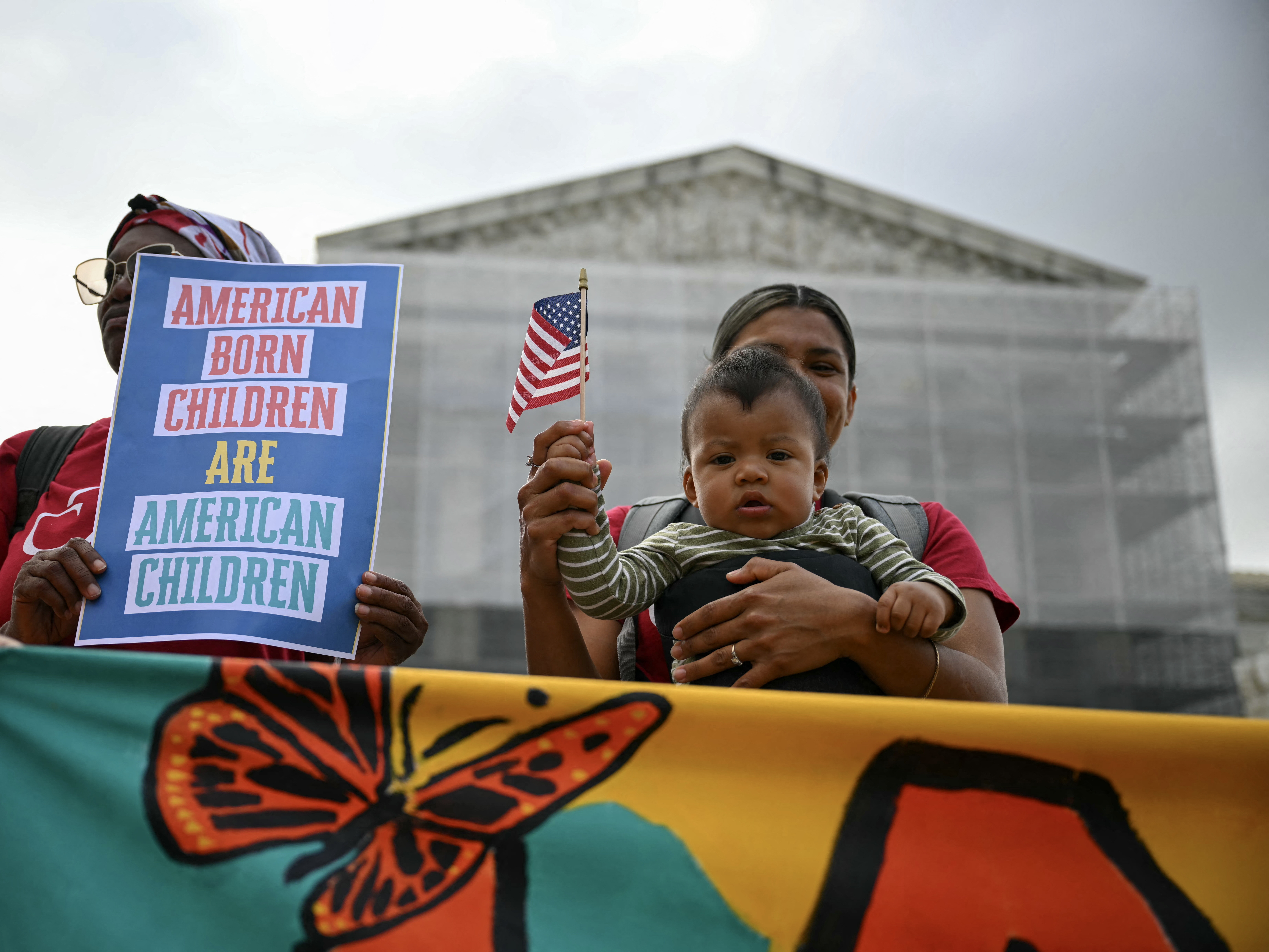 caption: Olga Urbina holds her 9-month-old son, Ares Webster, at a protest outside the U.S. Supreme Court in Washington, DC, in May 2025.