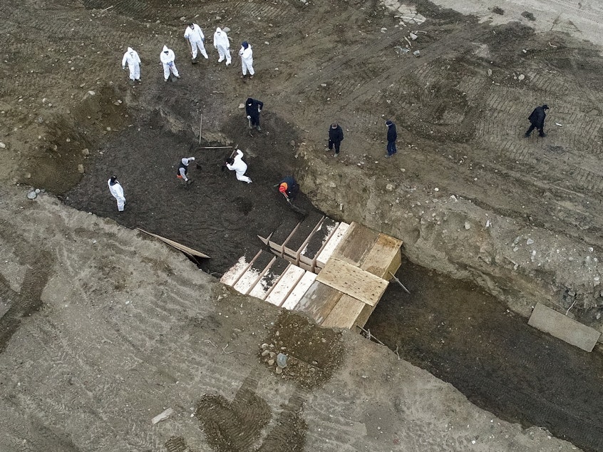 caption: Workers wearing protective gear bury bodies in a trench on Hart Island in New York City on April 9.