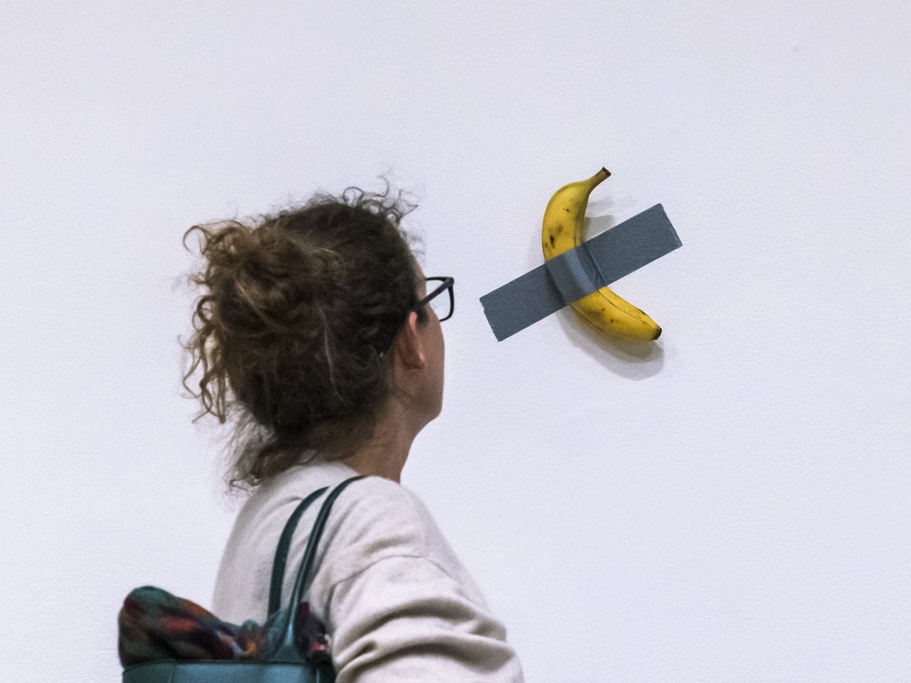 caption: A woman looks at artist Maurizio Cattelan's piece of art <em>Comedian</em> during an auction preview at Sotheby's in New York on Nov. 11, 2024.