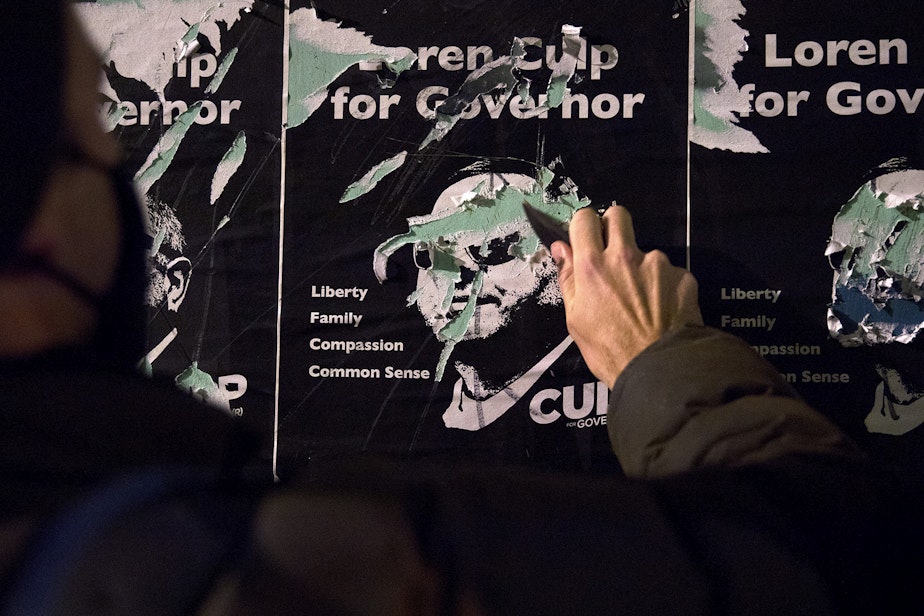 caption: A protester scratches the face of Loren Culp on a set of flyers with a knife as hundreds marched through the Pioneer Square neighborhood during a march focusing on counting every vote and protecting every person on Wednesday, November 4, 2020, in Seattle.