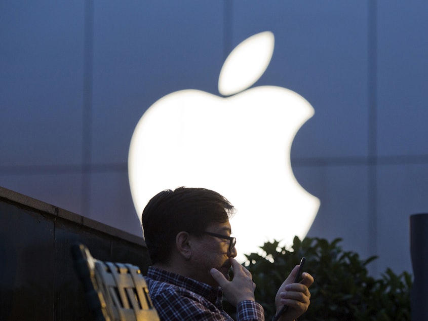 caption: A man uses his mobile phone near an Apple store logo in Beijing.