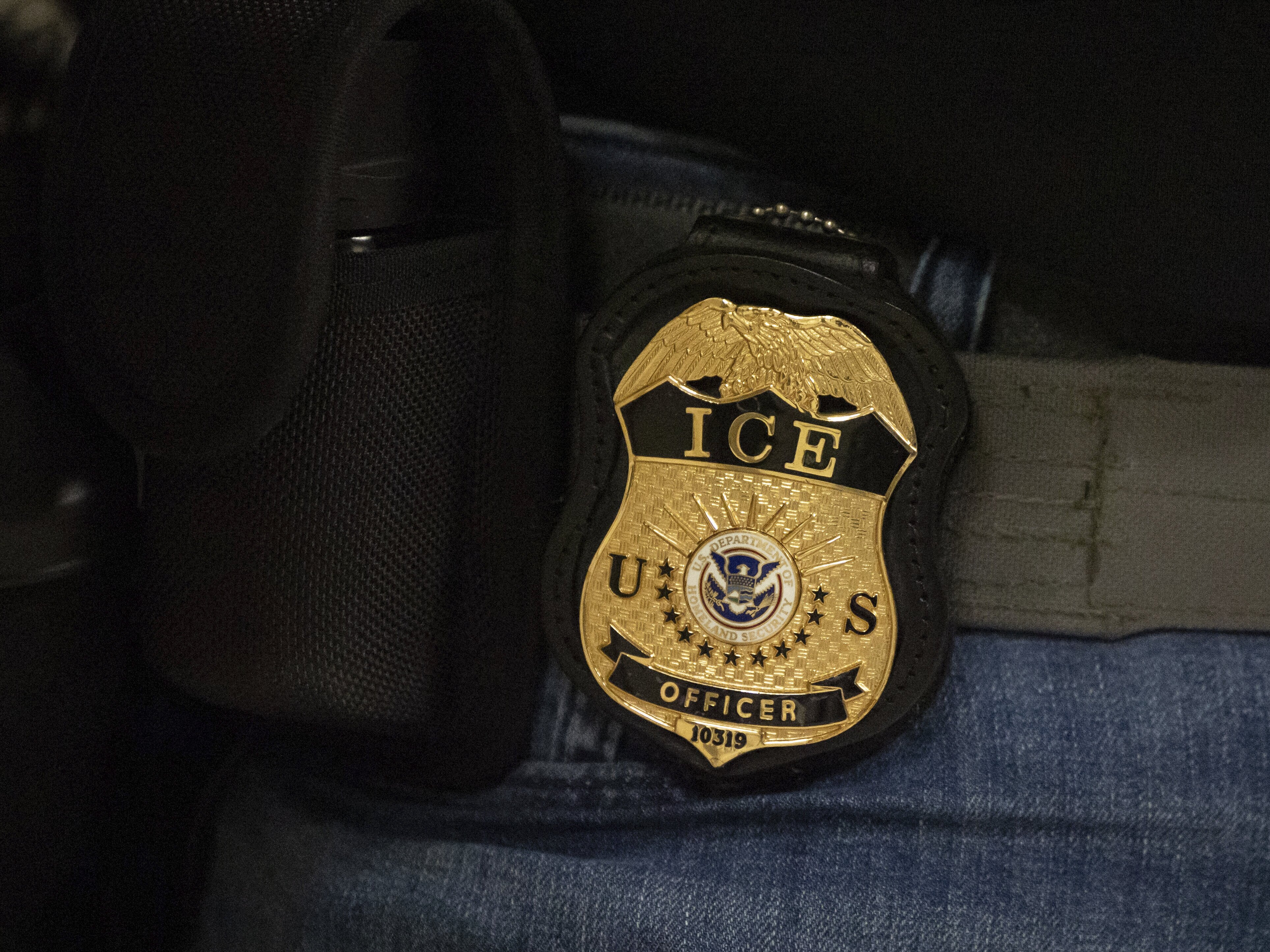 caption: A federal agent wears a badge of Immigration and Customs Enforcement while standing outside an immigration courtroom at the Jacob K. Javits Federal Building in New York City, on June 10.